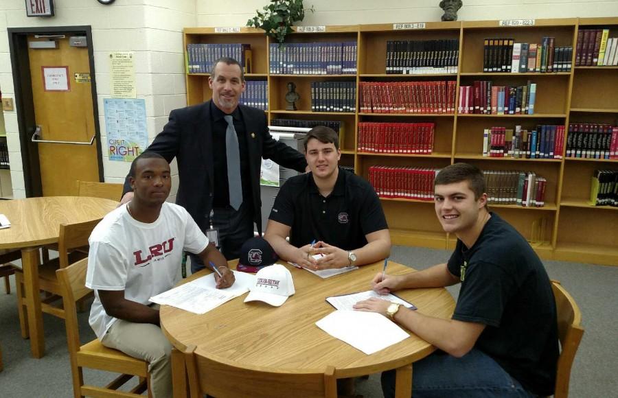 SENIOR FOOTBALL PLAYERS (L-R) Bradley Jones, Blake Camper, and Perry Schrader, with Head Football Coach Bill Stachelski  prepare to sign to their [respective] colleges.