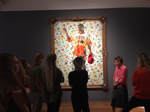 STUDENTS OBSERVE A painting while a curator gives insight on it.