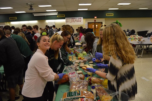 JUNIOR OLIVIA MCNULTY gives a helping hand at the #lunchbag event last year.  Students were lined up along the cafeteria tables in an assembly line to complete the desired goal.