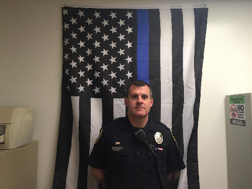OFFICER MARK WALBLAY stands proudly in front of his thin blue line American flag in his office. The thin blue line honors fallen officers and shows support for the living officers and their relations with the public.