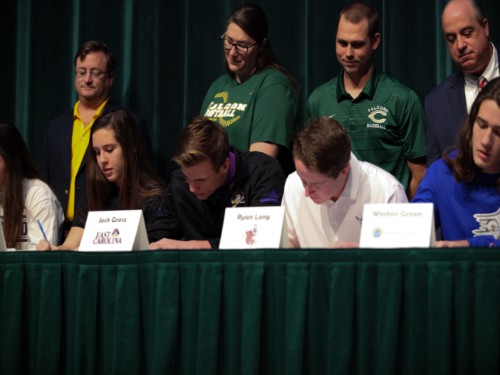 SENIORS SIGN TO commit to their college sports team. Their coaches stand proud behind them.
