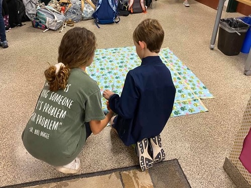 SENIOR AINSLEY ISENHOUR shows her middle school partner how to make a quilt. The quilts will go to those in need sometime in March.