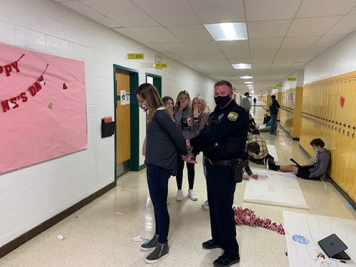 SCHOOL RESOURCE OFFICER Moran (left) puts the cuffs on those who dont obey the law both in and out of school. Students look on in disbelief as one of the teachers is caught while incorrectly directing students in her class.