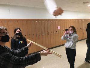 AP PHYSICS STUDENTS junior Cassi Martin and seniors  Evi Capetanakis and Evan Spencer use a meter stick to determine the centripetal force of the flying pig. The pig flys around to give the students live practice at measuring. 