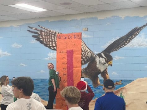 JUNIOR RACHEL HOLROYD takes a picture beside the total board. This years goal was to make 1,200 bagged lunches in 60 minutes, which they happily surpassed.