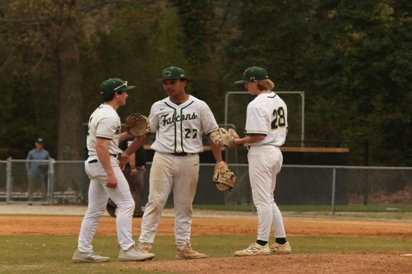 FALCON BASEBALL PLAYERS meet at the mound for an intense conversion about the previous play's outcome. The boys are trying to give the pitcher some extra advice.